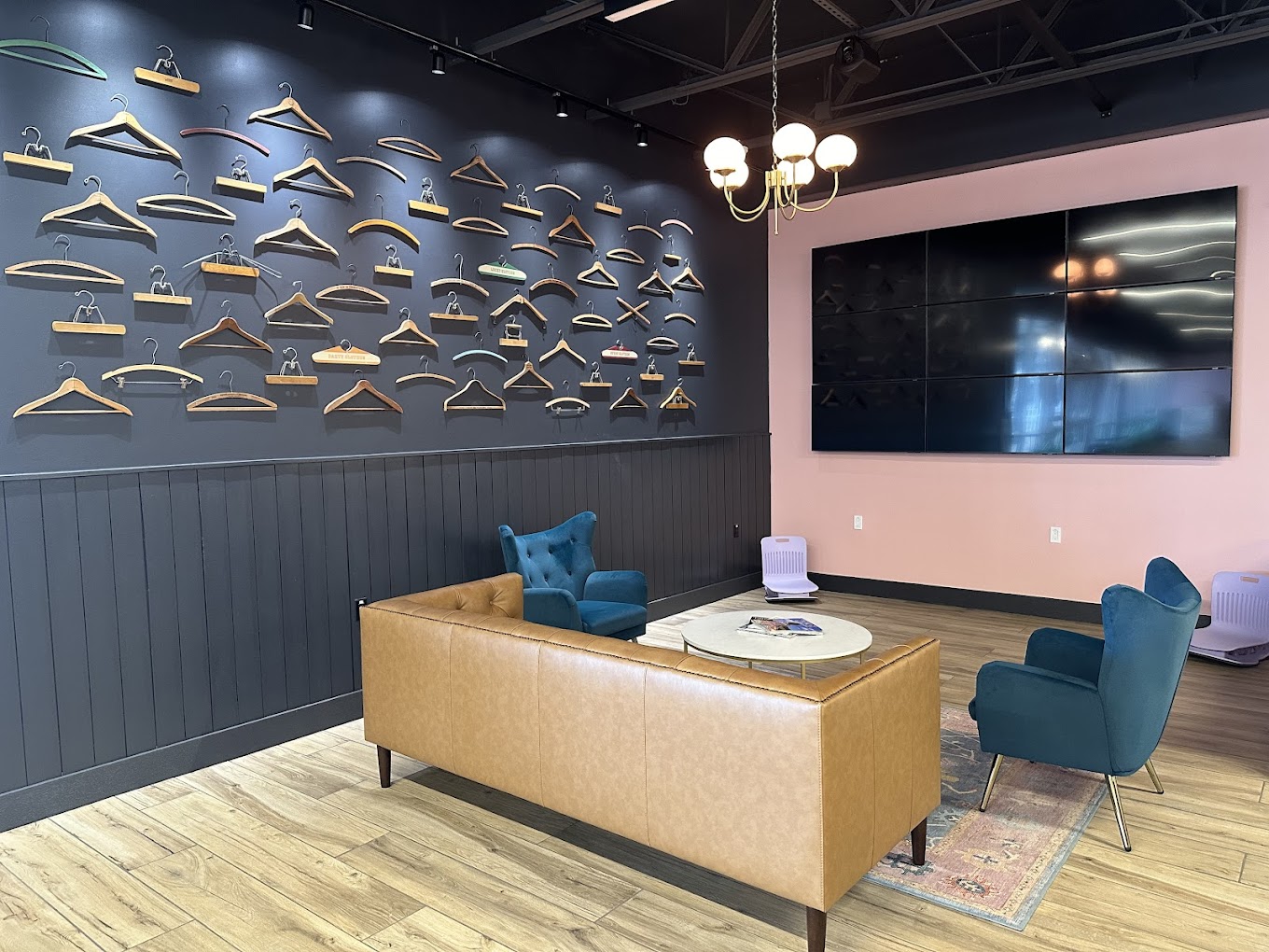 Gold hanger sculpture wall above a tan leather sofa and teal armchairs